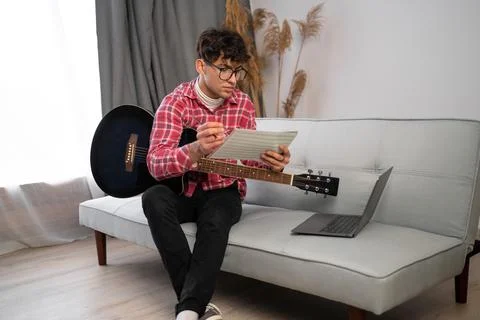 Young arabic composer man composing song using guitar and laptop at home si.. Stock Photos