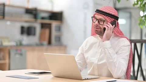 Young Arabic Man with Laptop Talking on Smartphone in Office Stock Footage 139775833