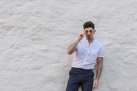 Young arabic man looking at camera through sunglasses in white shirt standing Stock Photos