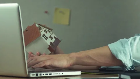Young architect creating housing project on laptop holding house model in hand Stock Footage 81880478