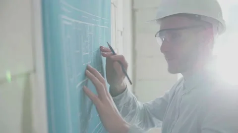 Young architect engineer works with blueprints  in a helmet and glasses Video stock 133056633