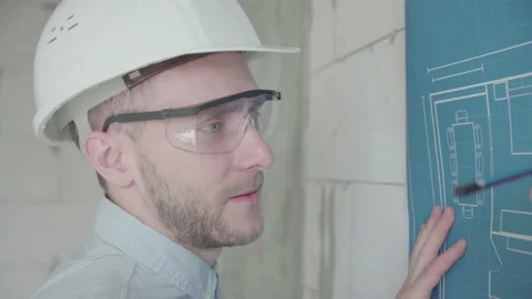Young architect engineer works with blueprints  in a helmet and glasses Video stock 133073607