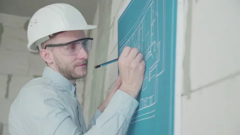 Young architect engineer works with blueprints  in a helmet and glasses Video stock 133073715