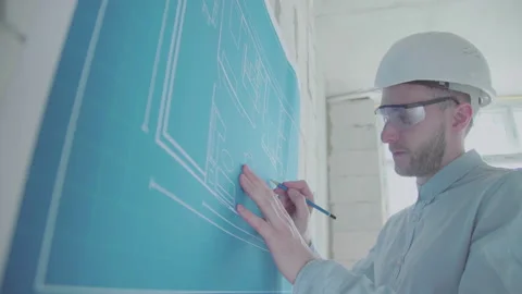 Young architect engineer works with blueprints  in a helmet and glasses Video stock 133073718