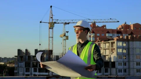 A young architectural engineer in a protective helmet and vest looks Stock Footage 128630863