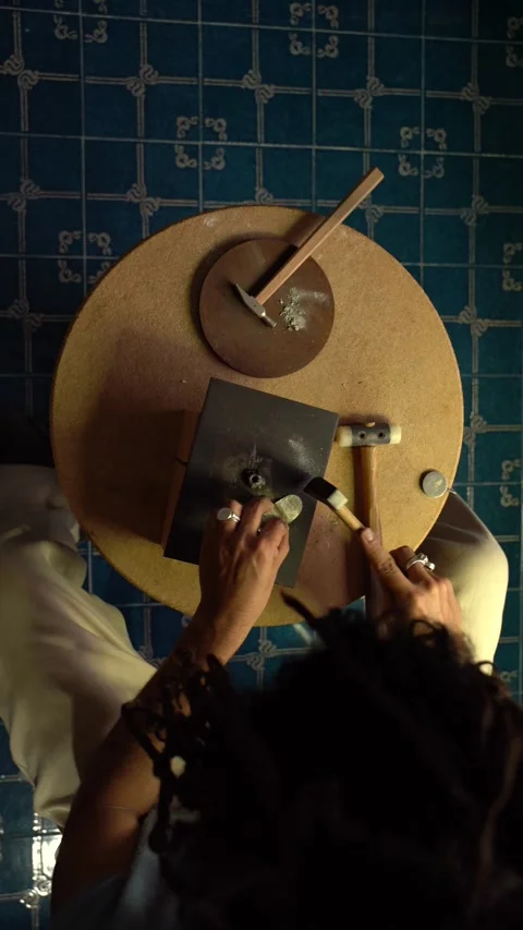 Young artisan hammering brass sheet in the making of a piece of jewelry. Go.. Video stock 253390233