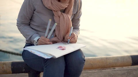 A young artist is engaged in drawing while waiting for her friends and the sea Stock Footage 90306664