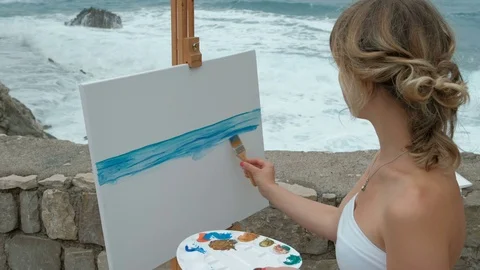 Young artist on the shore of the surging waves in writing seascape. Stock Footage 77329161