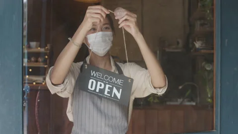 Young Asia girl wear face mask turning a sign from closed to open sign on door. Stock Footage