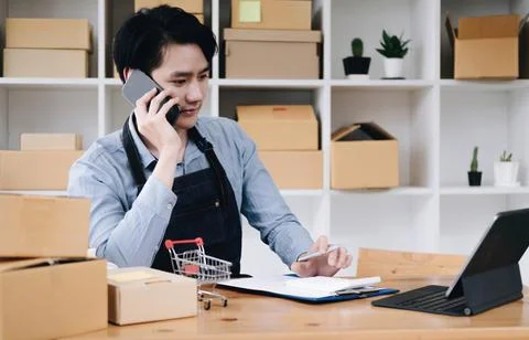 Young asia seller man happy work on laptop busy cellphone call chat to customer Stock Photos