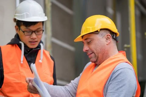 Young Asian apprentice at work on construction site with senior engineer Stock Photos