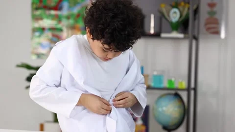 Young Asian Boy Buttoning Up White Lab Coat in Science Classroom Stock Footage 328139237
