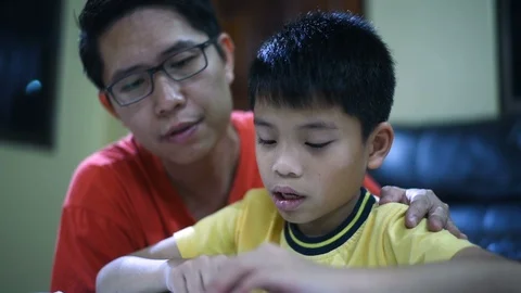 Young Asian boy doing his school homework with his father, at home, he is readin Stock Footage 105085170