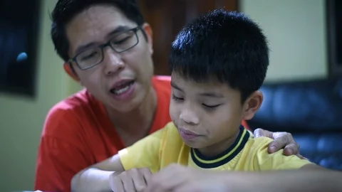 Young Asian boy doing his school homework with his father, at home, he is readin Stock Footage 105085875