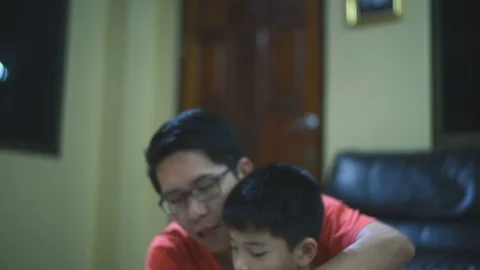 Young Asian boy doing his school homework with his father, at home, he is readin Stock Footage 105175604