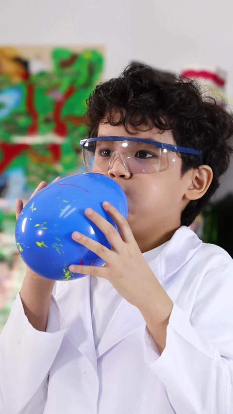 Young Asian Boy in Lab Coat Blowing Up Blue Balloon Video stock 338155510