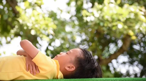 Young Asian boy lay down and wake up on the green lawn in the park Video stock 58168996