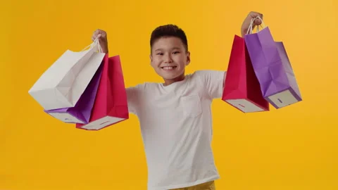 Young asian boy smiling and raising hands with multicolor paper bags in both Stock Footage 246712656