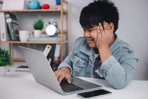 Young Asian boy smiling while using a laptop at his desk, representing succ.. Stock-Fotos