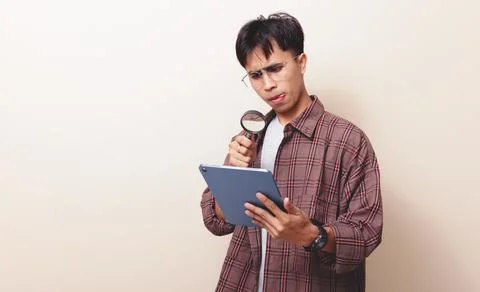Young asian businessman using tablet and magnifying glass with focused expr.. Stock Photos