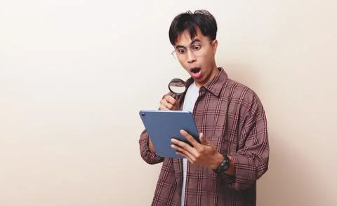 Young asian businessman using tablet and magnifying glass, showing surprise.. Stock Photos