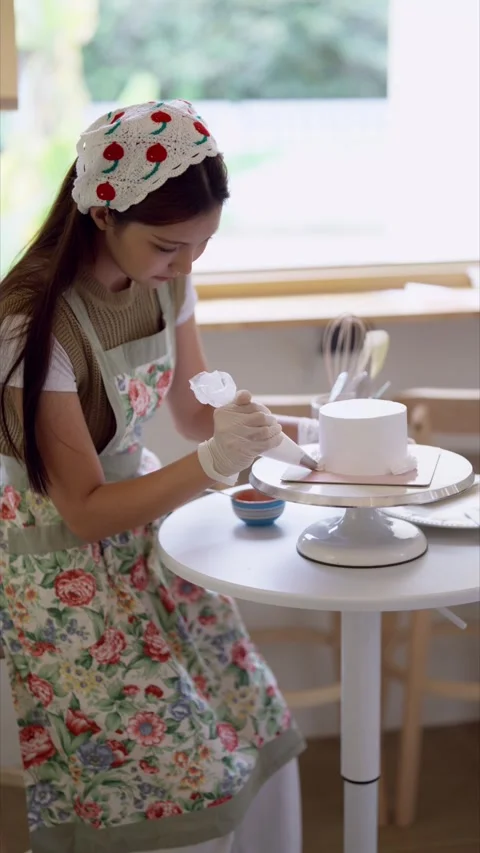 Young Asian cake decorator smoothing buttercream frosting on white cake wit.. Stock Footage 345102640