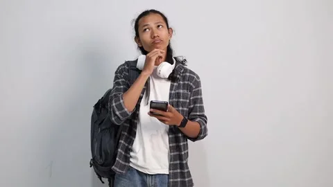 Young asian college student texting while thinking of message reply on white Stock Footage 319807299