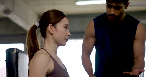 Young Asian couple exercising in modern gym, woman performs seated dumbbell curl Stock Footage 337648931
