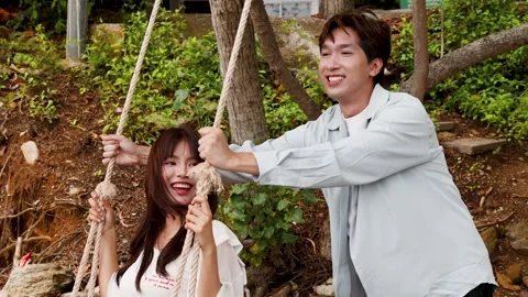 Young Asian Couple Having Fun on Wooden Swing Outdoors Stock Footage 345784009
