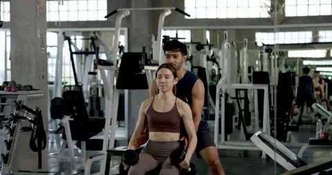 Young Asian couple practicing seated dumbbell lateral raise in modern gym, man 스톡 동영상 342587237