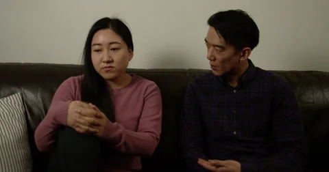 A young asian couple sitting on the couch and arguing over a disagreement. Stock Footage 58742532