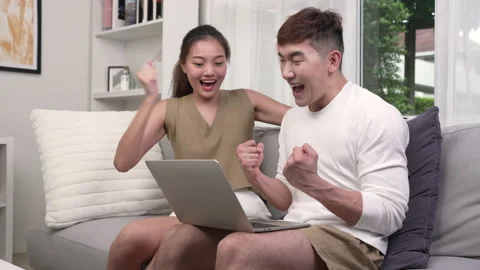 Young Asian couple using computer laptop in the living room and celebrating Stock Footage 218575977
