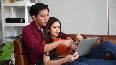 Young asian couple using notebook or laptop for online shopping in living room Stock Footage 122379485