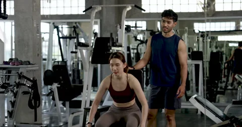 Young Asian couple working out in modern gym, woman seated with dumbbells while Stock Footage 337650994