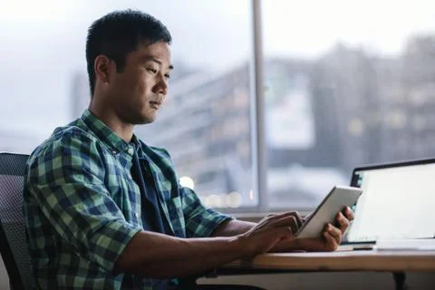 Young Asian designer using a tablet at his office workstation Stock Photos