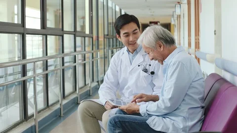 Young asian doctor talking to senior male patient in hospital hallway Stock Footage