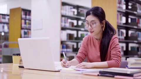 Young Asian female student using laptop computer writing notes studying res.. Stock Footage 335003356