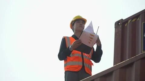 Young asian foreman checking list on clipboard talking on the walkie-talkie c Stock Footage 157716500