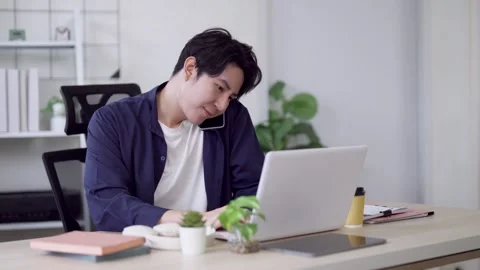Young Asian freelancer multitasking with phone call while working on laptop.. Stock Footage 337650527