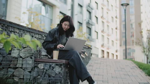 Young asian freelancer working remotely on laptop and drinking coffee outdoors Stock Footage 295143349