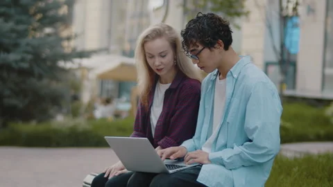 Young asian guy with a laptop sitting on a bench outdoors on a city street and Stock Footage 278323727