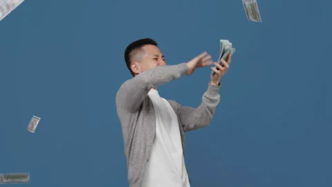 Young asian guy with an overjoyed face throws banknotes around from the stack in Stock Footage 254896632