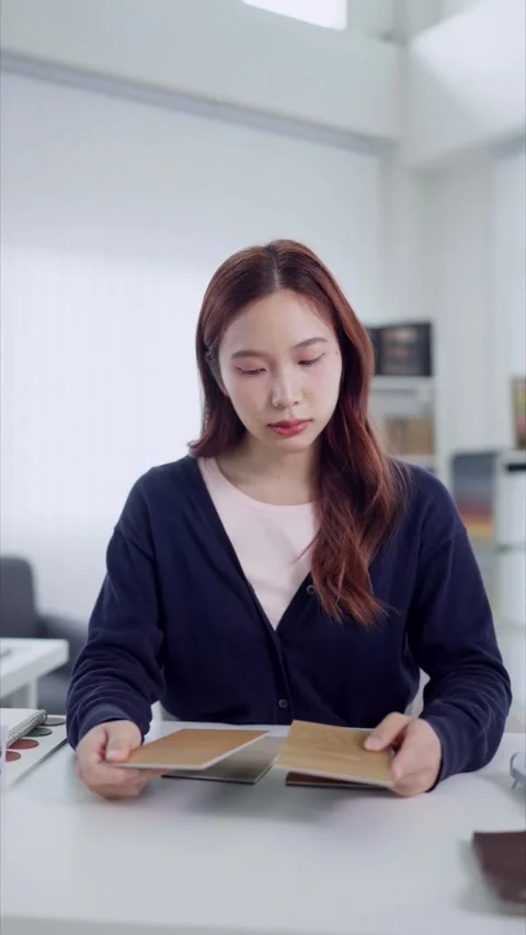 Young Asian interior designer comparing wood veneer swatches at desk in bri.. Stock Footage 345149254