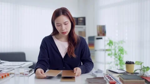 Young Asian interior designer examines wood veneer swatches while working a.. Stock Footage 345149233