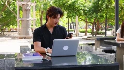 Young Asian Male Student Using Smartphone and Laptop on University Campus Stock Footage 327885605