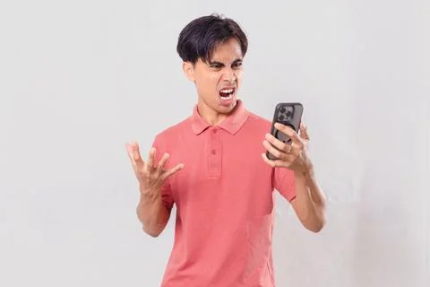 Young Asian man angrily using his mobile phone, isolated on plain backgroun.. Stock Photos