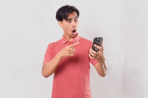 Young Asian man angrily using his mobile phone, isolated on plain backgroun.. Stock Photos