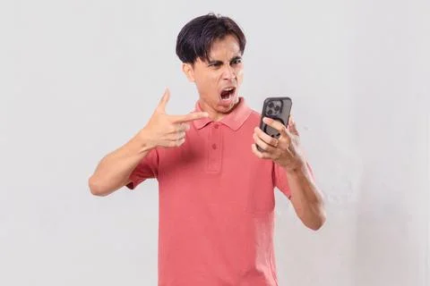Young Asian man angrily using his mobile phone, isolated on plain backgroun.. Stock Photos