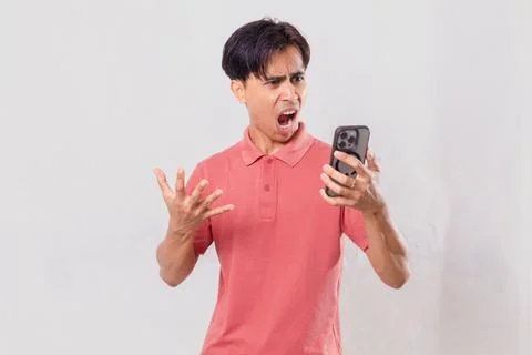 Young Asian man angrily using his mobile phone, isolated on plain backgroun.. Stock Photos