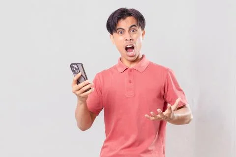 Young Asian man angrily using his mobile phone, isolated on plain backgroun.. Stock Photos